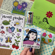 Load image into Gallery viewer, A hand holds a die-cut sticker featuring a retro-style girl with dark hair and a pink polka-dot top with the text 'it's cool to care!' surrounded by butterflies. The background is a styled flat-lay of various 'secret garden' themed stickers, stamps, and a green envelope.
