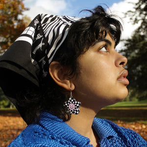 Photograph of a young woman's side profile, she is looking up to the sky wearing the bandana and a checkered daisy earring.