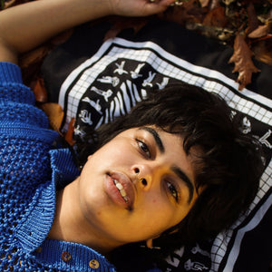 Photograph of woman laying on the ground, looking into the camera. She is laying her head on the bandana.